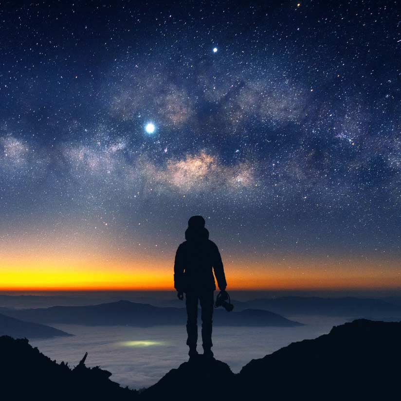 Photographe, appareil à la main , devant un ciel étoilé avec coucher de soleil